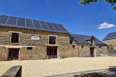 Cour extérieure ensoleillée avec des tentes noires, des fleurs en pot et une maison en pierre en arrière-plan.