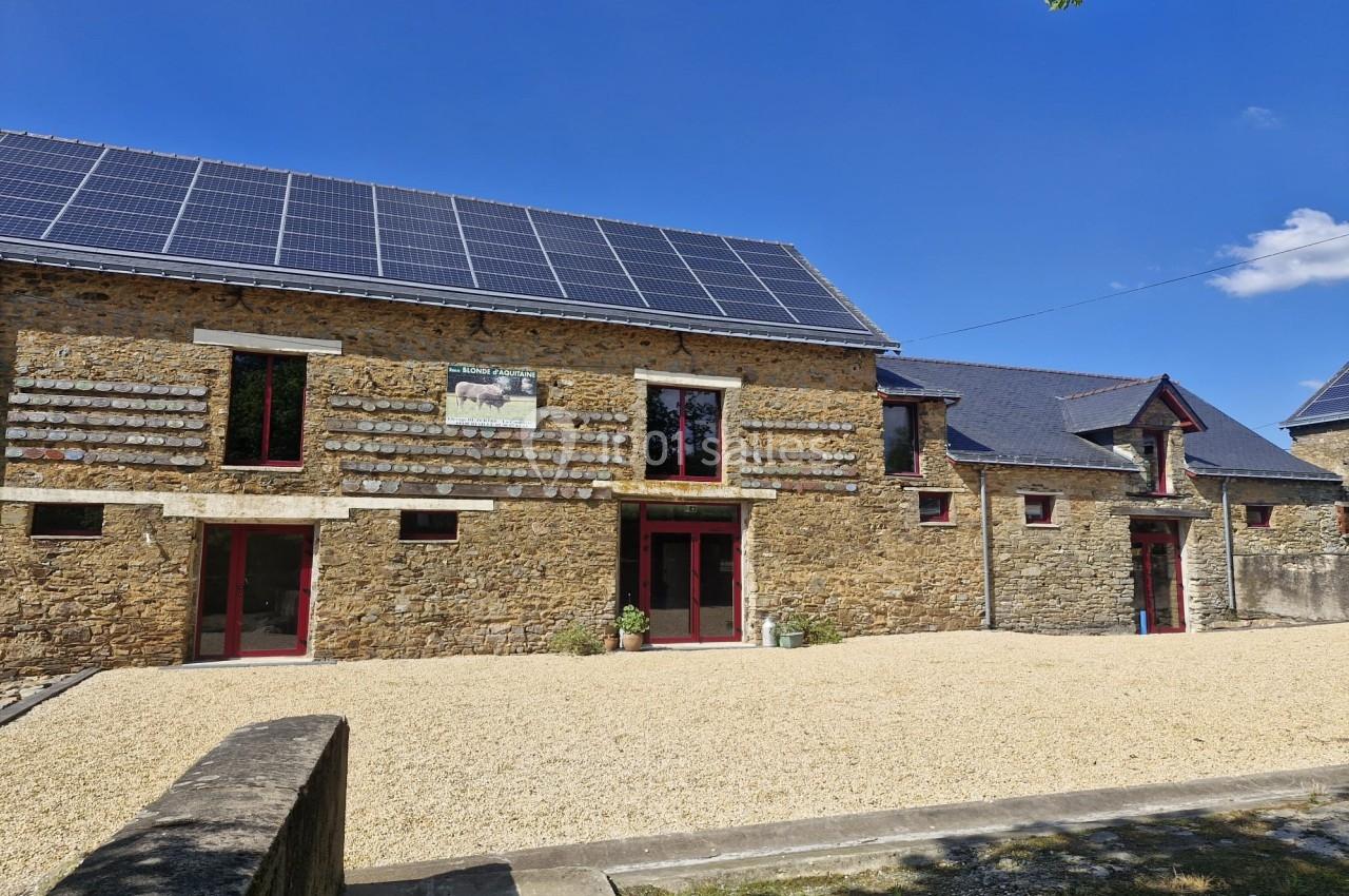 Façade en pierre d'un bâtiment rural rénové avec panneaux solaires sur le toit et cour en gravier.
