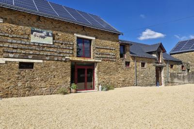 Cour extérieure ensoleillée avec des tentes noires, des fleurs en pot et une maison en pierre en arrière-plan.