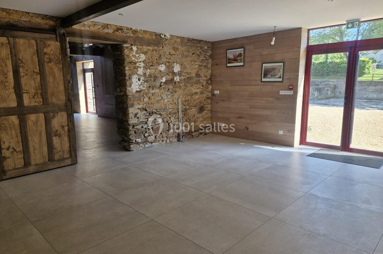 Salle lumineuse avec murs en pierre et bois, carrelage clair, grande baie vitrée et porte coulissante en bois.