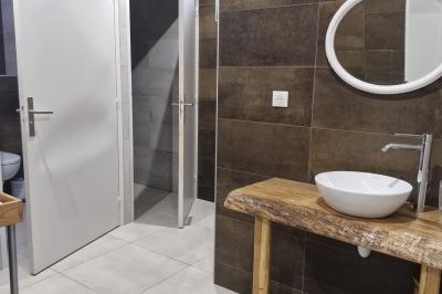 Cour extérieure ensoleillée avec des tentes noires, des fleurs en pot et une maison en pierre en arrière-plan.