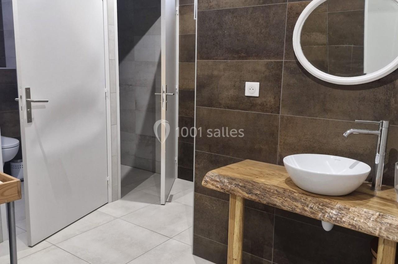 Salle de bain moderne avec lavabo sur meuble en bois, miroir rond et murs en carrelage foncé.