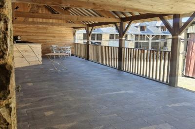 Cour extérieure ensoleillée avec des tentes noires, des fleurs en pot et une maison en pierre en arrière-plan.