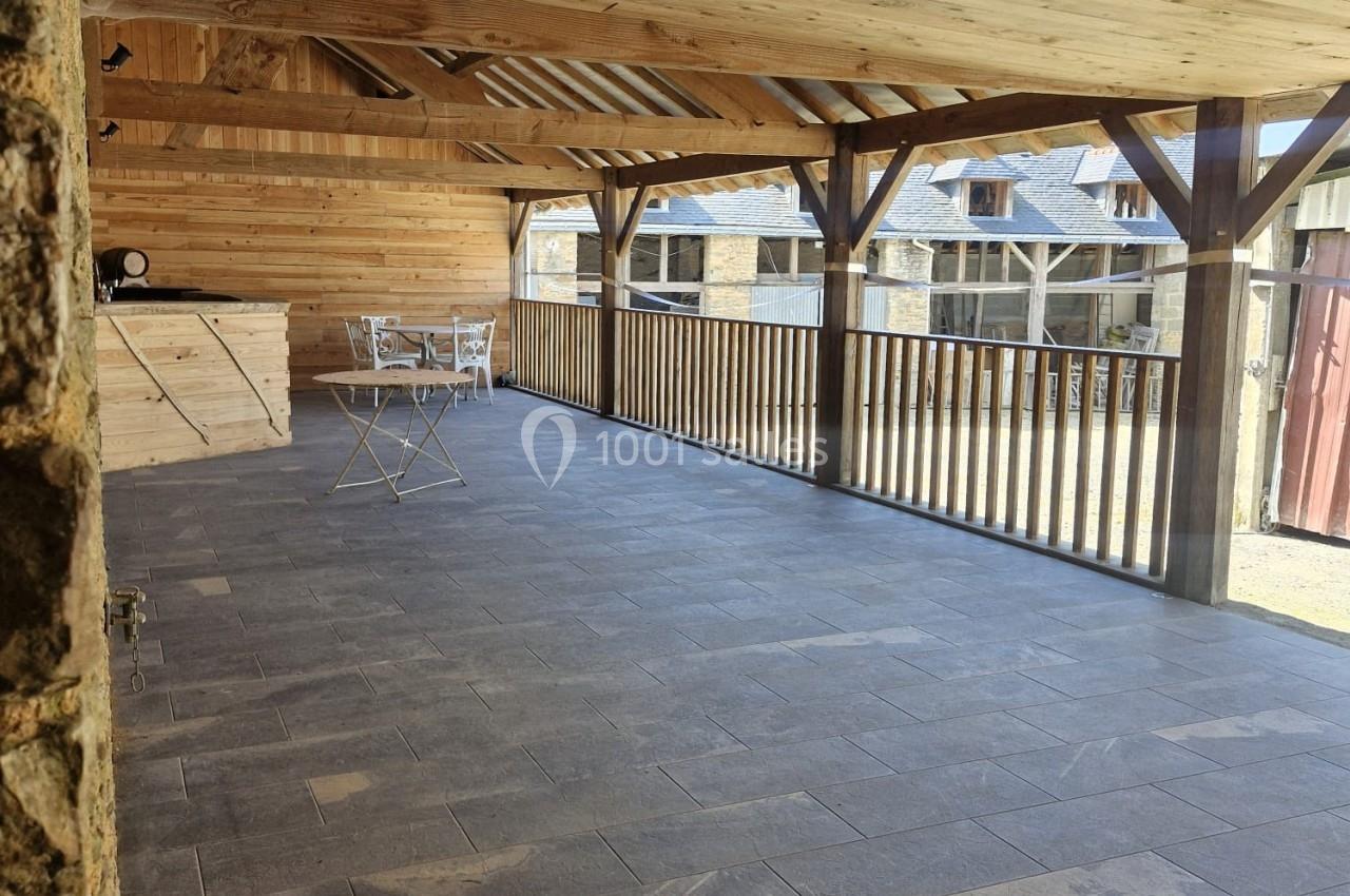 Terrasse couverte en bois avec sol en pierre, équipée d'une table et de chaises, donnant sur des bâtiments voisins.