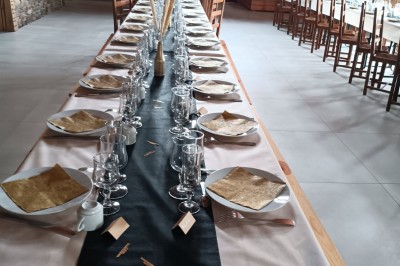 Cour extérieure ensoleillée avec des tentes noires, des fleurs en pot et une maison en pierre en arrière-plan.