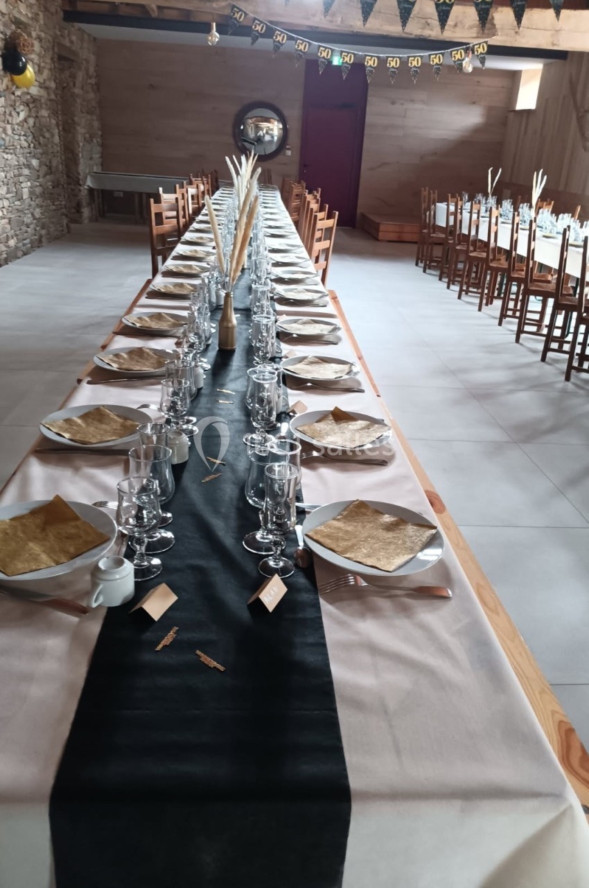 Grande table de banquet décorée avec nappes, vaisselle et marque-places, dans une salle en pierre et bois.