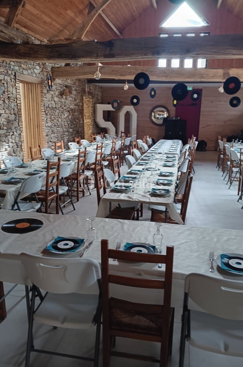 Salle décorée pour une fête, avec longues tables dressées, disques vinyles en décoration et le chiffre 50 en arrière-plan.