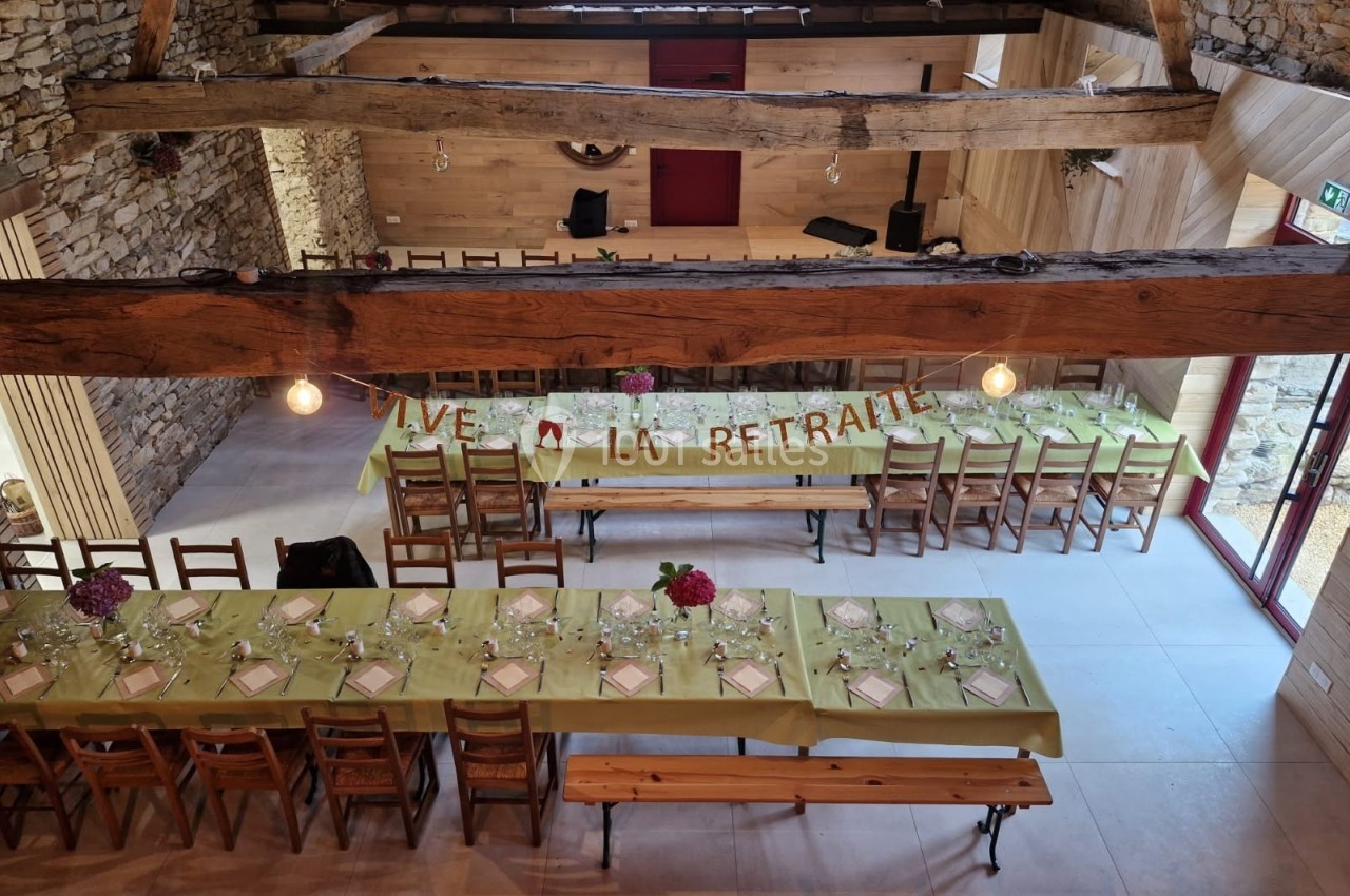 Salle décorée pour une fête, avec de longues tables dressées, une bannière ’Vive la retraite’ et des murs en pierre…