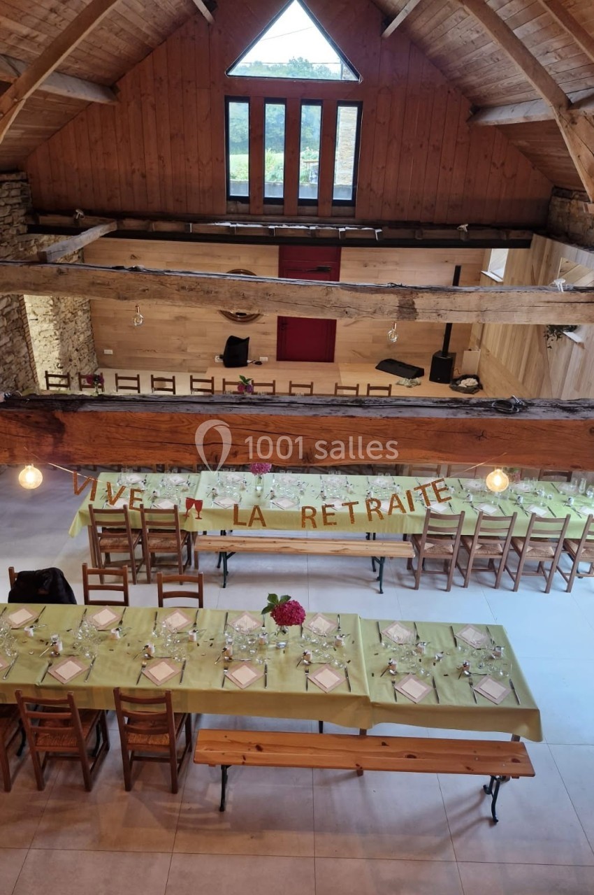 Salle en bois avec des tables décorées pour une fête, une bannière ’Vive la retraite’ accrochée en arrière-plan.