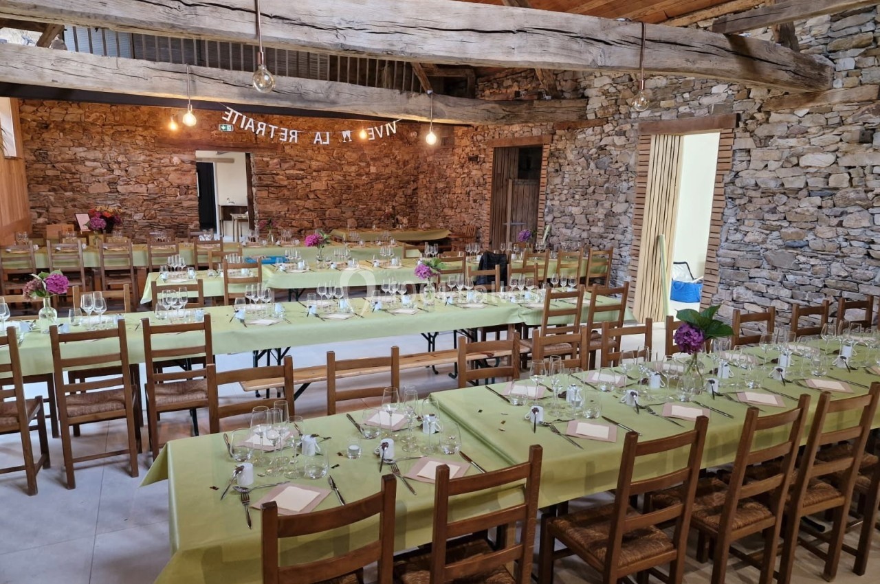 Salle rustique avec murs en pierre, tables alignées couvertes de nappes vertes, dressées pour un repas festif.
