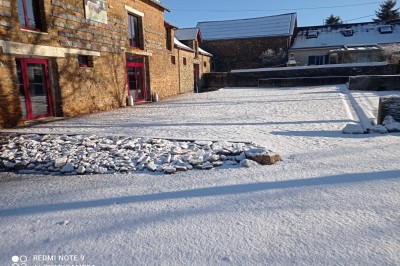 Cour enneigée entourée de bâtiments en pierre avec des fenêtres rouges, sous un ciel dégagé ensoleillé.