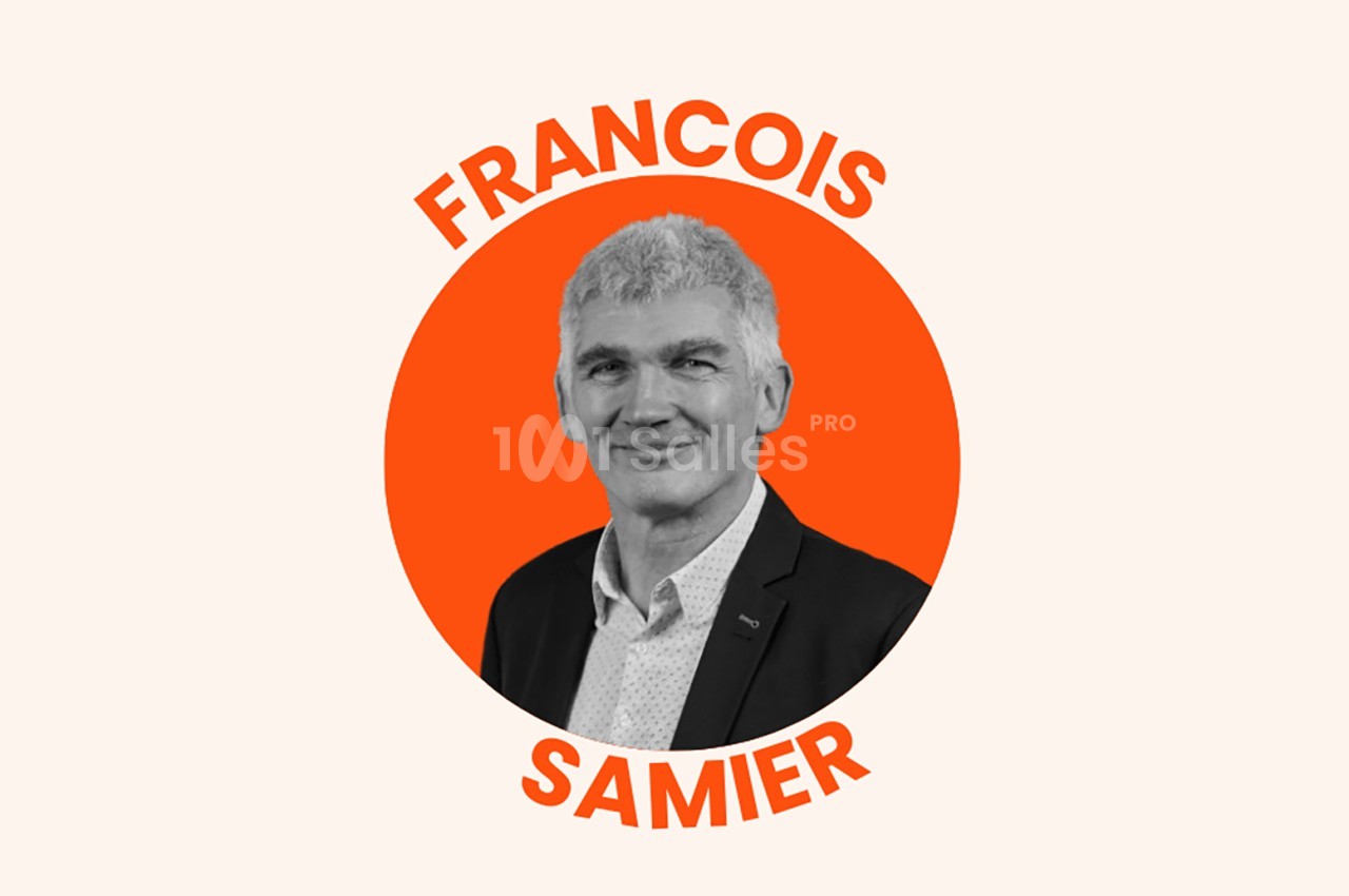 Portrait en noir et blanc d'un homme souriant en costume, sur un fond orange circulaire avec son nom inscrit autour.