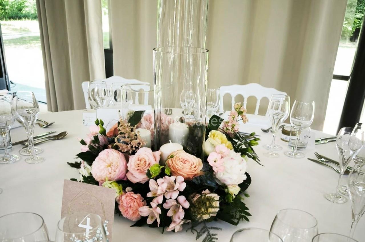 Centre de table floral avec roses et bougies dans un vase en verre, entouré de couverts sur une nappe blanche.