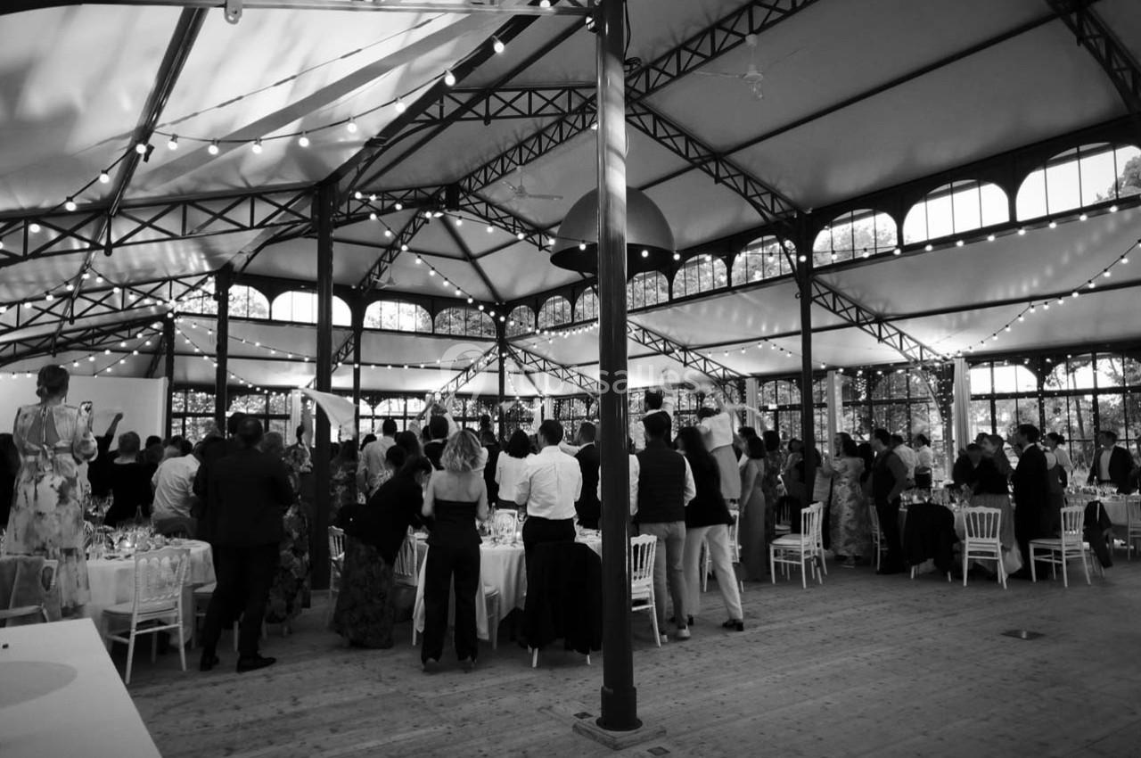 Salle de réception avec des invités debout sous une structure métallique, éclairée par des guirlandes lumineuses.