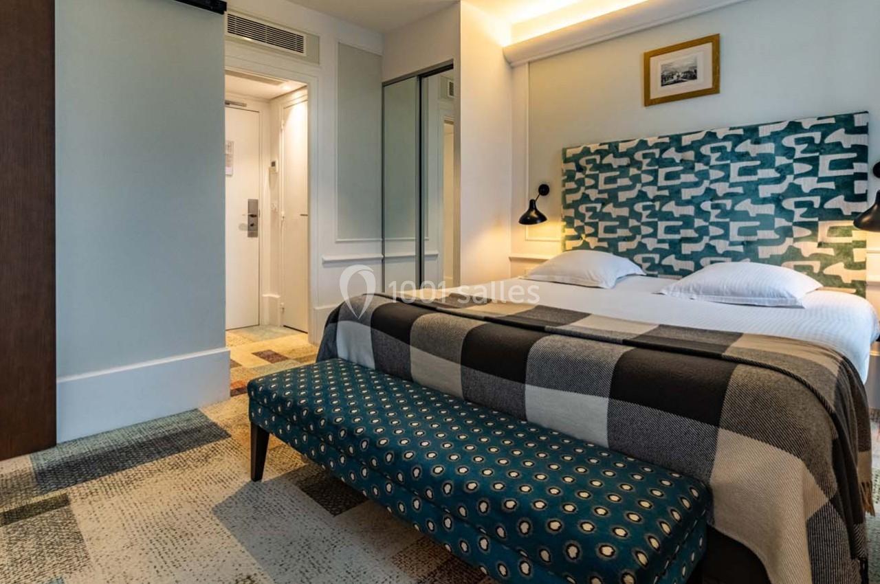 Chambre d'hôtel avec lit double, tête de lit graphique, banc rembourré, éclairage mural et sol en motifs variés.