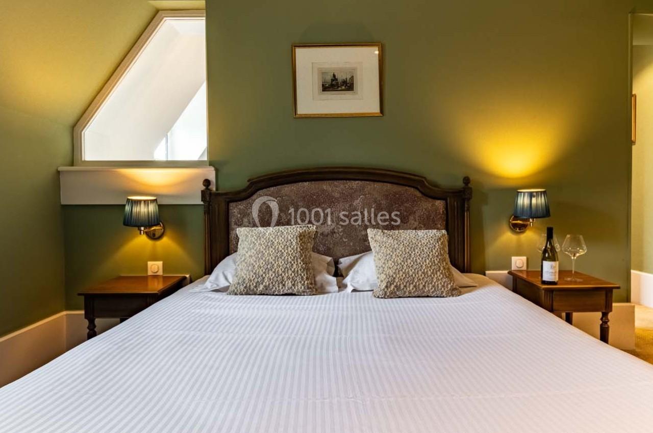 Lit double avec tête de lit en bois, deux tables de chevet, lampes allumées et bouteille de vin dans une chambre verte.