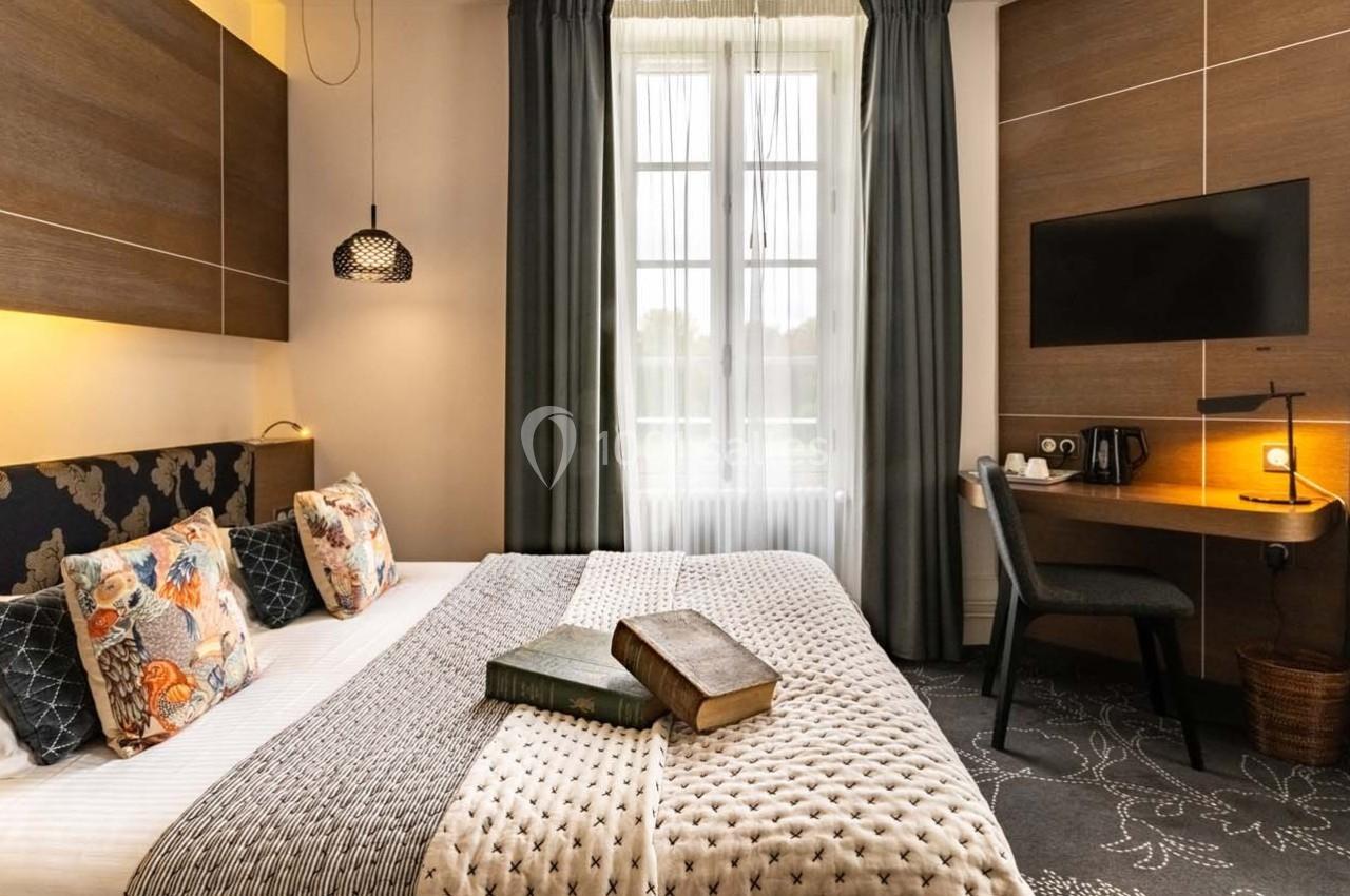 Chambre d'hôtel avec lit double, coussins décoratifs, bureau, télévision murale et fenêtre avec rideaux.