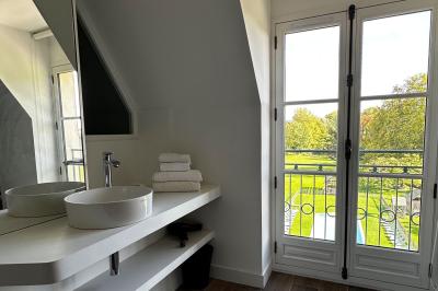 Salle de bain lumineuse avec vasque blanche, serviettes pliées et vue sur un jardin à travers une porte-fenêtre.