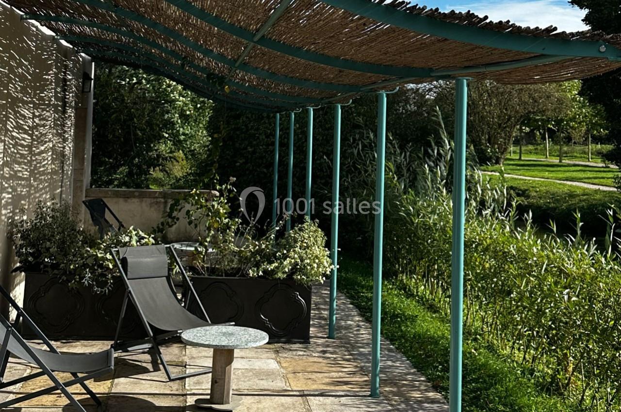 Terrasse ombragée avec pergola en canisse, chaises longues, table basse et vue sur un jardin verdoyant.
