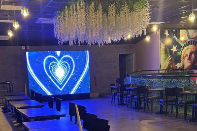 Salle moderne avec écran affichant des cœurs lumineux, tables et chaises noires, plafond décoré de fleurs suspendues.