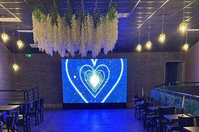 Salle moderne avec écran affichant des cœurs lumineux, tables et chaises noires, plafond décoré de fleurs suspendues.