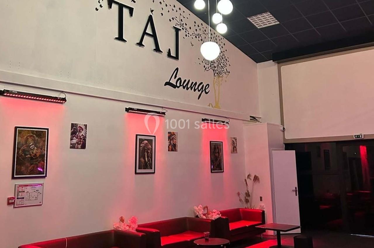 Espace intérieur d'un salon avec canapés rouges, murs décorés de tableaux et enseigne ’Taj Lounge’ éclairée.