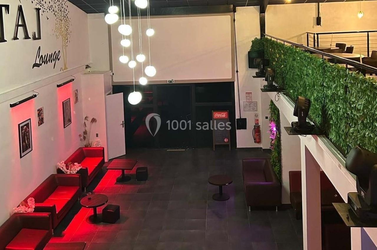 Vue intérieure d'un salon moderne avec canapés rouges, éclairage suspendu et mur végétal sur une mezzanine.