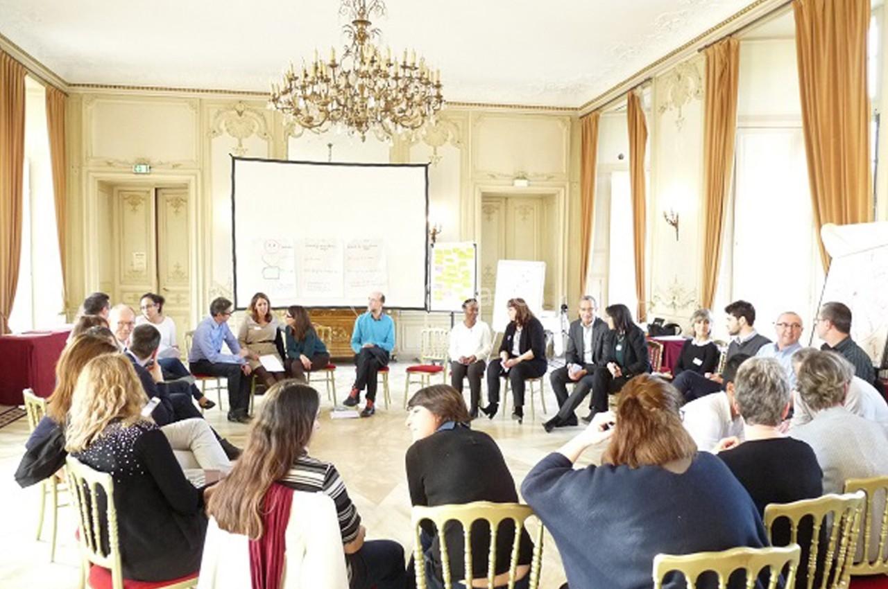 Un groupe de personnes assises en cercle dans une salle lumineuse avec un projecteur et des tableaux de présentation.