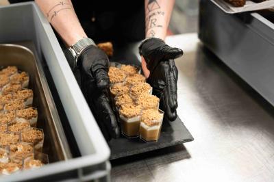 Miniature Cocktail verrines dessert Minutes Papillons Personne disposant des verrines individuelles garnies de crumble sur un plateau dans une cuisine professionnelle.