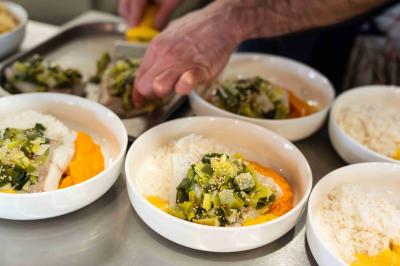 Miniature Menu cuisine Minutes Papillons Personne disposant des verrines individuelles garnies de crumble sur un plateau dans une cuisine professionnelle.