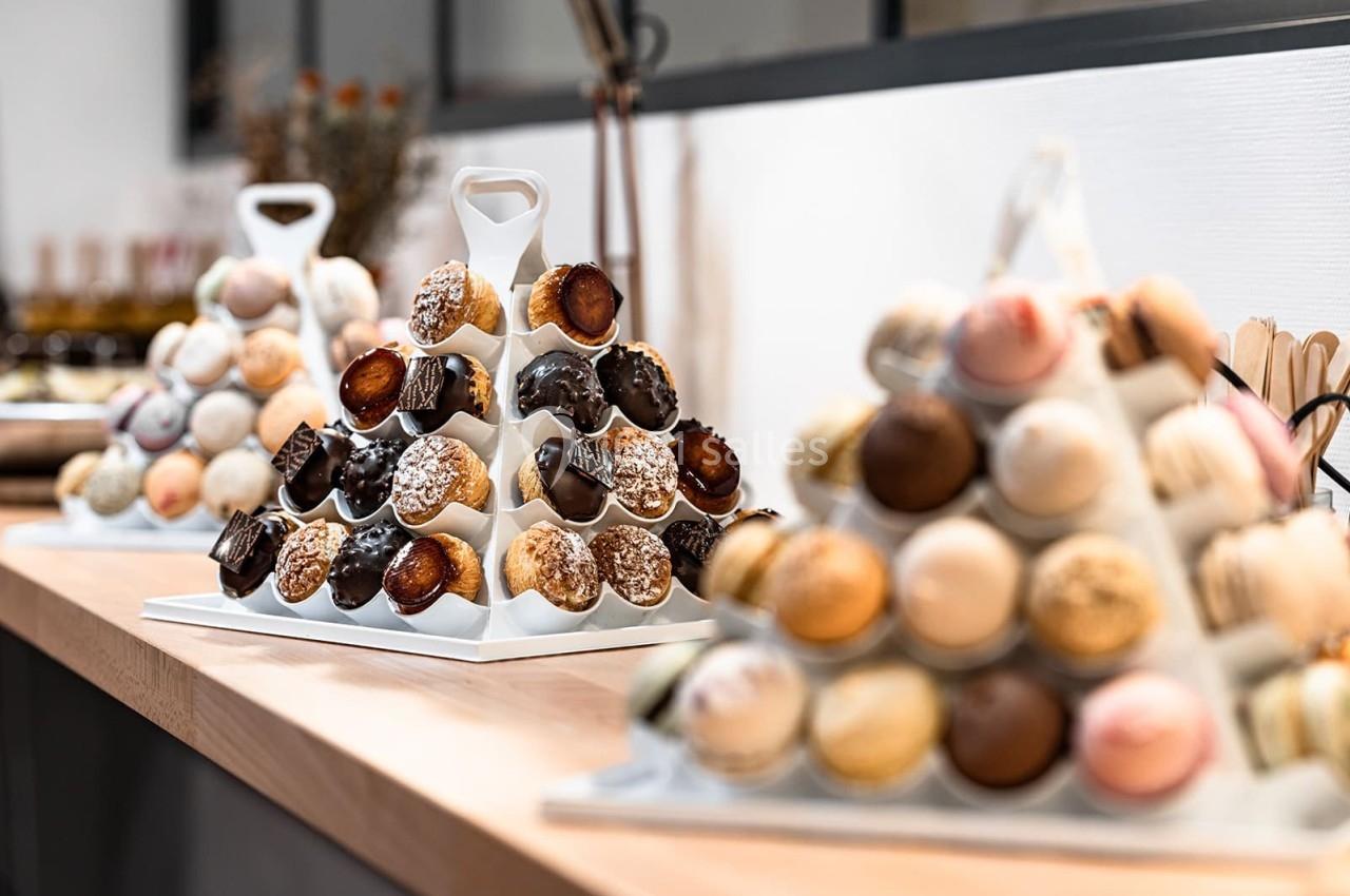 Plateaux de pâtisseries variées, dont des choux et macarons, disposés en pyramides sur un comptoir en bois.