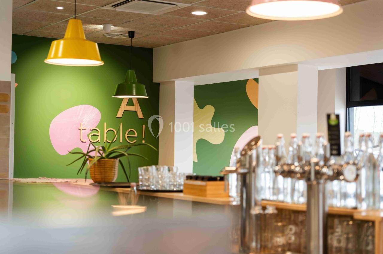Intérieur d'un café moderne avec un comptoir, des bouteilles en verre et un mur décoré de couleurs vives.
