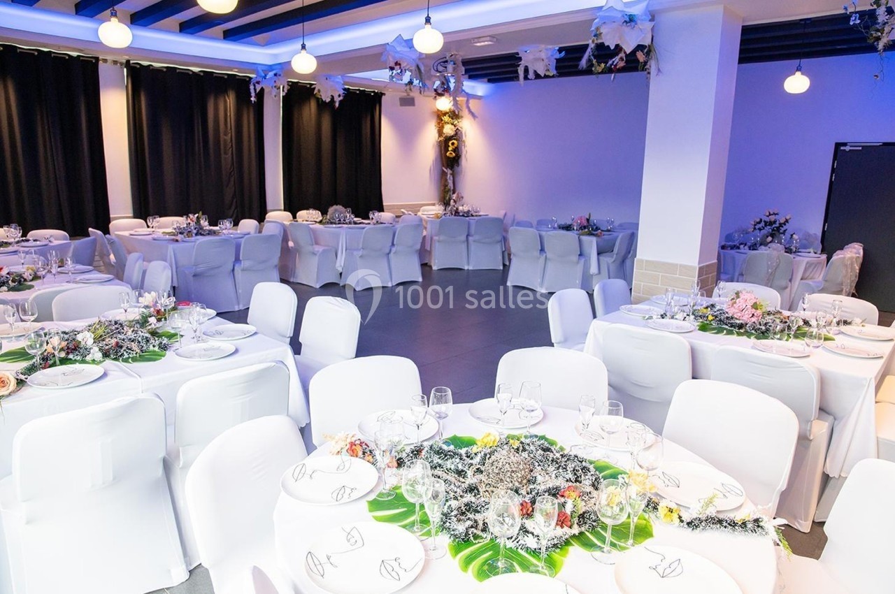 Salle de réception décorée avec des tables rondes dressées, nappes blanches et ornements floraux.