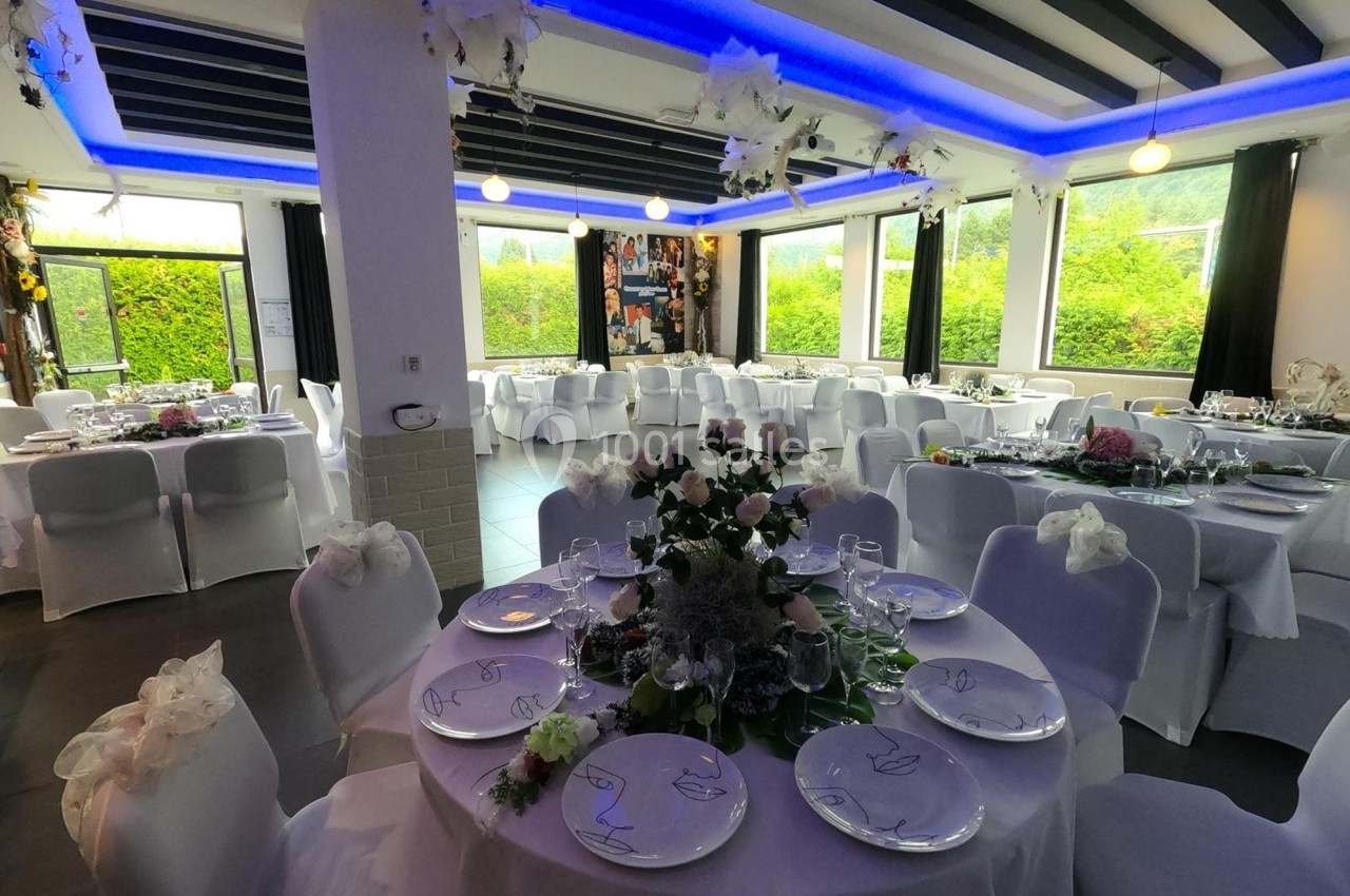 Salle de réception décorée avec des tables rondes dressées, nappes blanches et éclairage LED bleu au plafond.