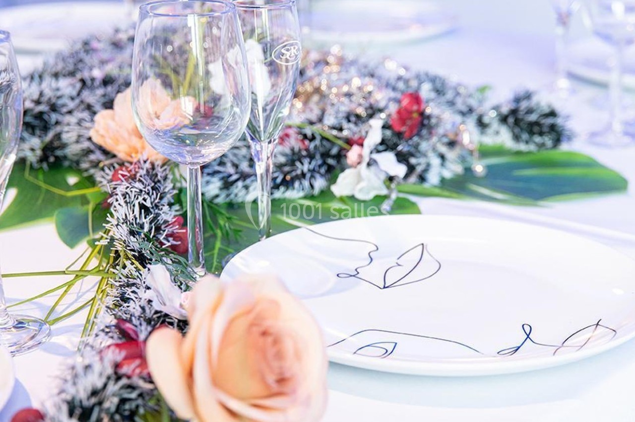 Table décorée avec des assiettes blanches, des verres et un centre de table floral avec des branches enneigées.