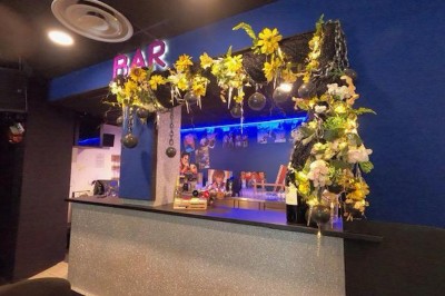 Miniature Location salle Cluses (Haute-Savoie) - Salle du Mont Blanc #19 Comptoir de bar décoré de guirlandes lumineuses, fleurs jaunes et blanches, avec un éclairage bleu en arrière-plan.