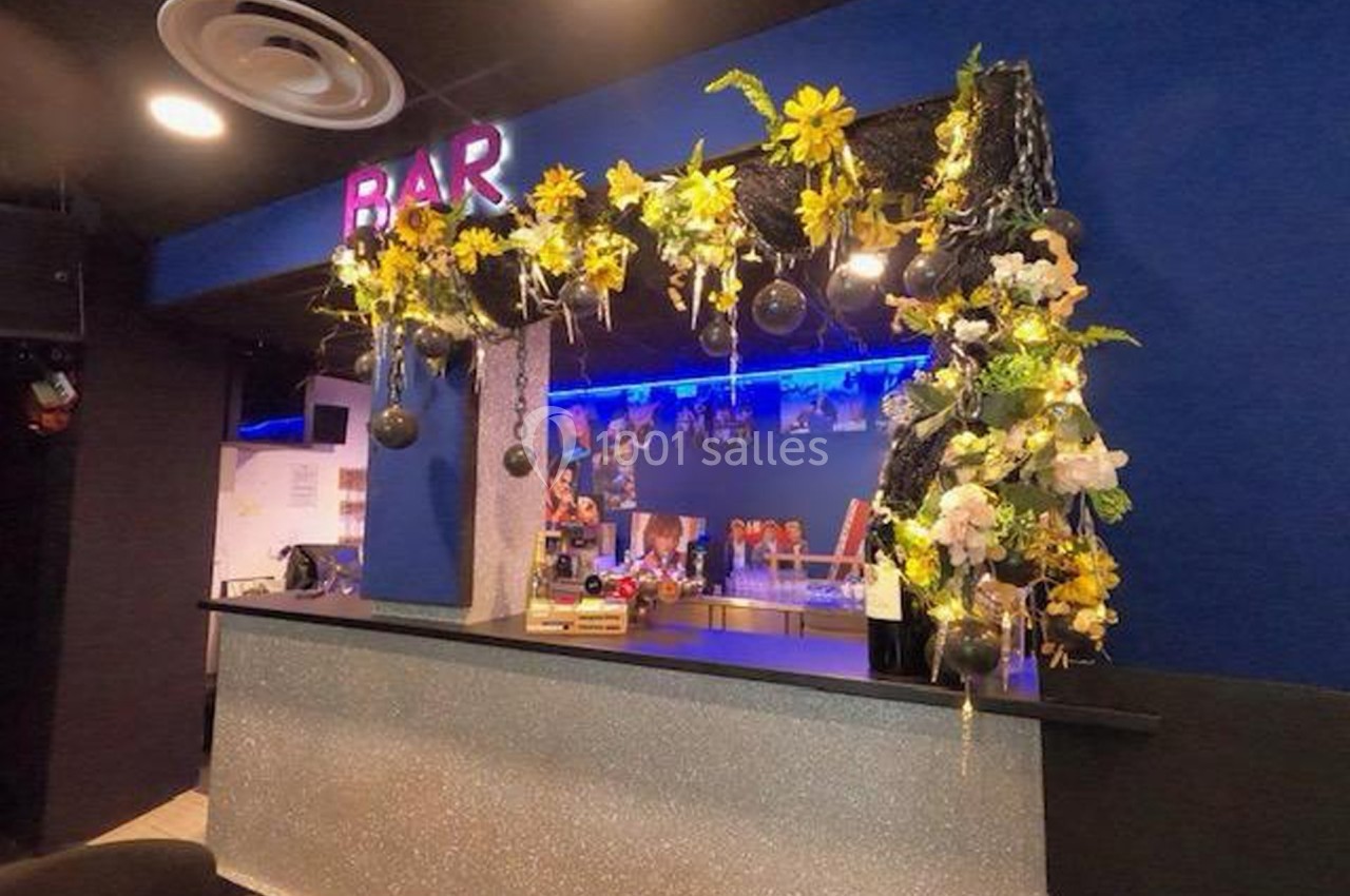 Comptoir de bar décoré de guirlandes lumineuses, fleurs jaunes et blanches, avec un éclairage bleu en arrière-plan.