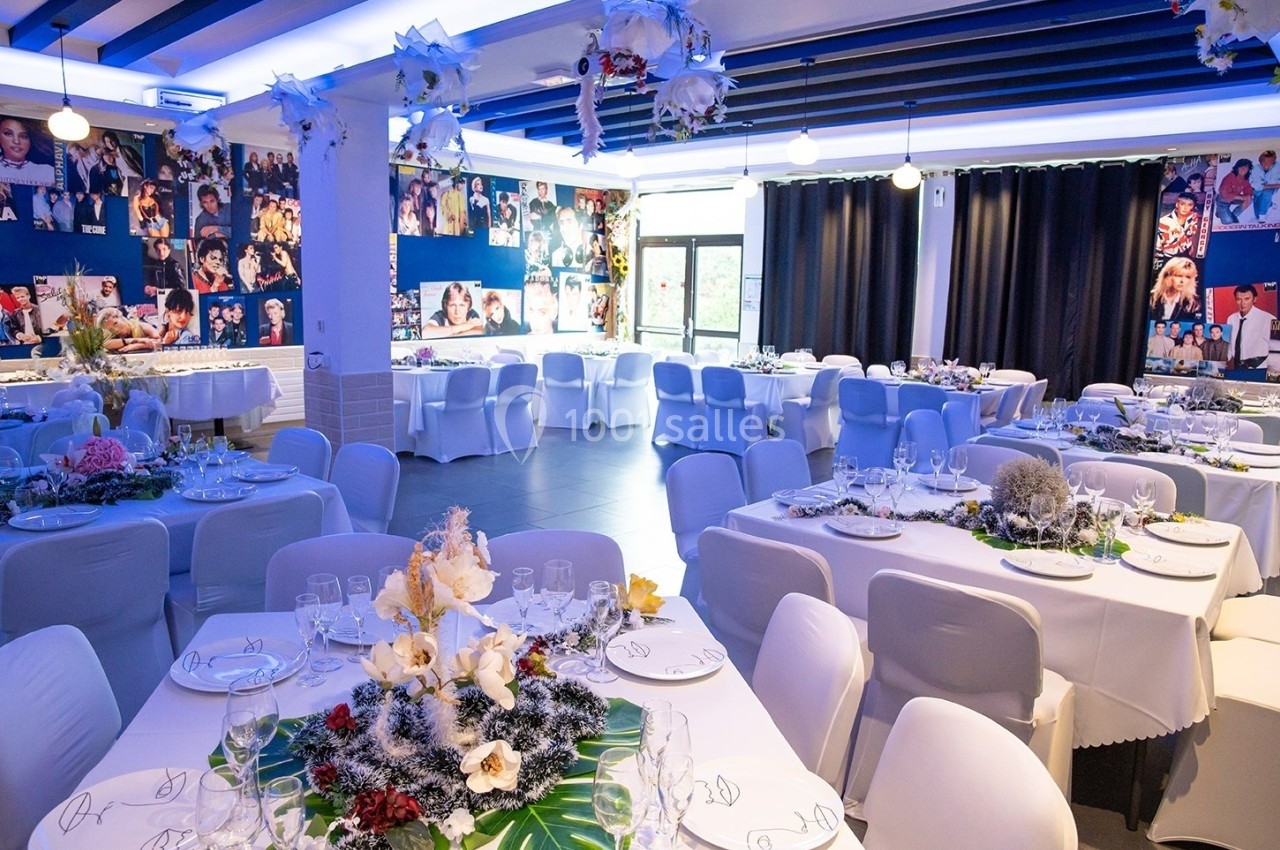 Salle de réception décorée avec des tables dressées, des fleurs et des photos accrochées aux murs.