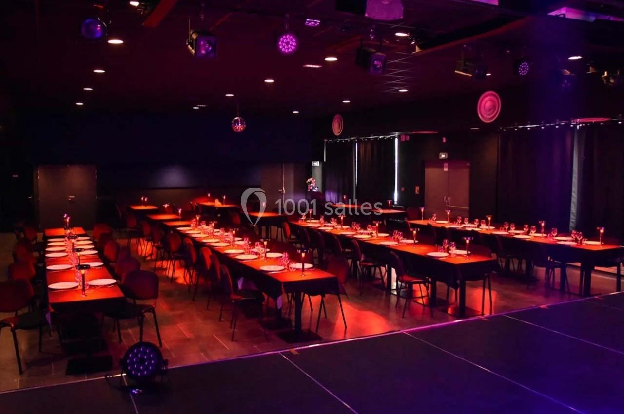 Salle de réception avec tables dressées, éclairage tamisé rouge et scène visible au premier plan.