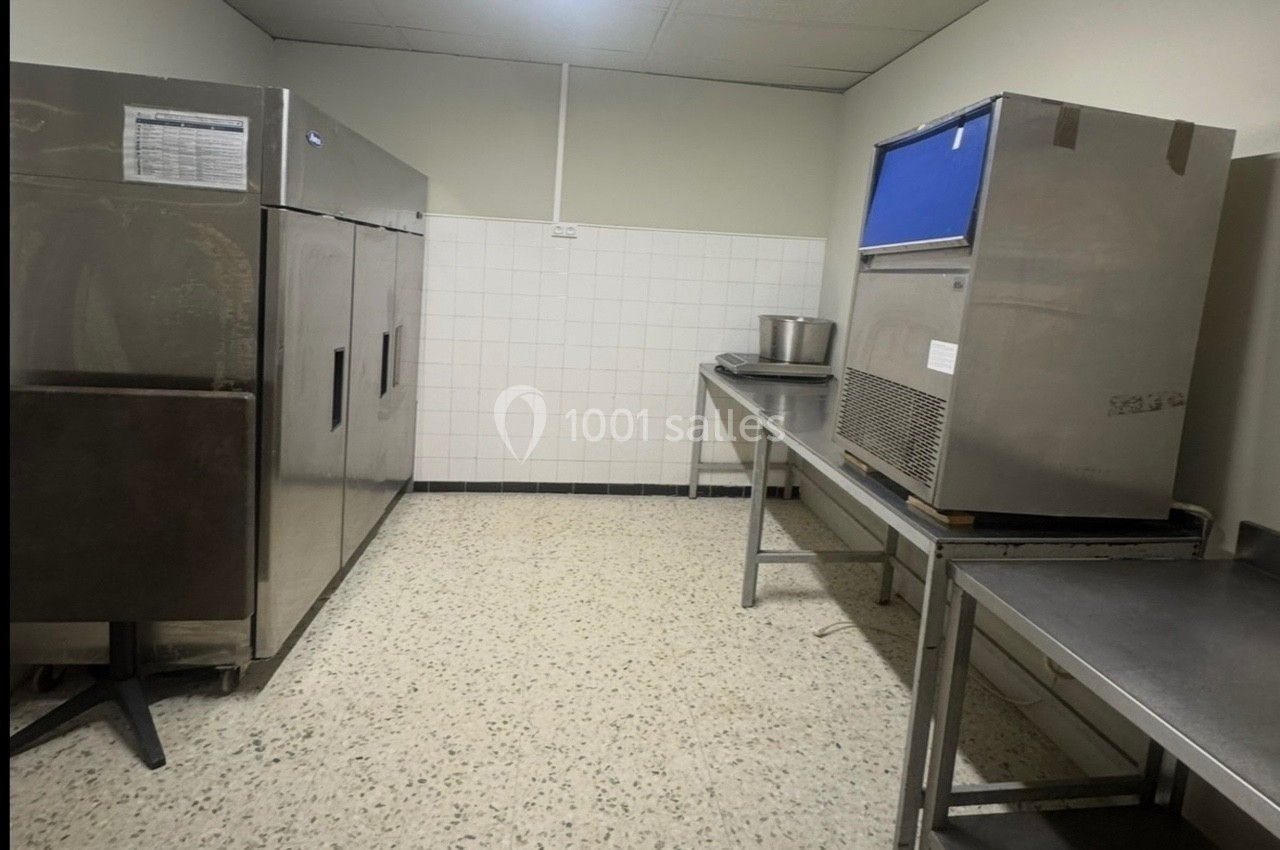 Salle de cuisine avec réfrigérateurs industriels, plan de travail en inox et sol en carrelage clair.