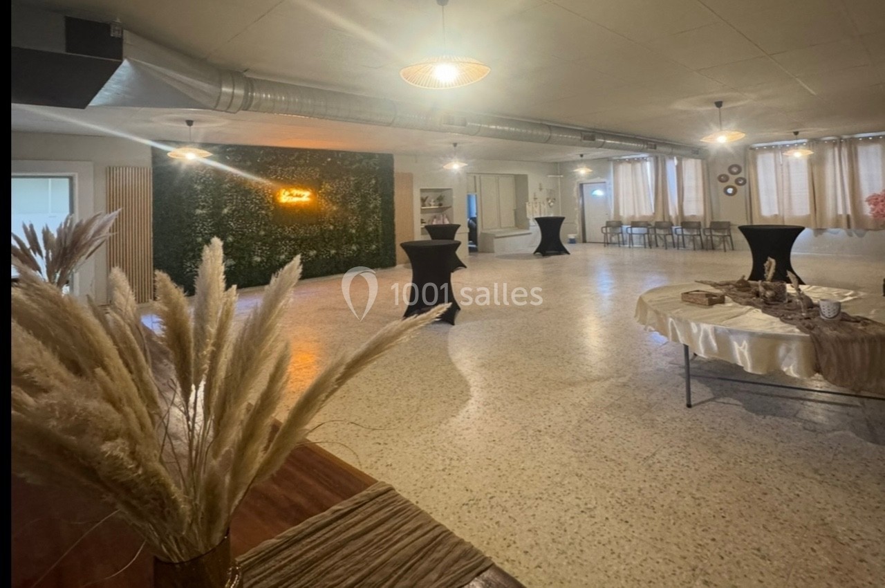 Salle lumineuse avec tables hautes, décoration végétale murale, pampas en premier plan et buffet dressé.