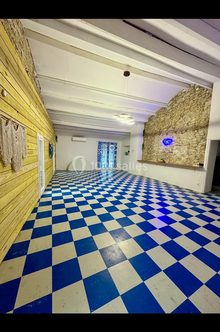 Salle intérieure avec sol en damier bleu et blanc, murs en pierre et bois, éclairage suspendu et décoration murale.
