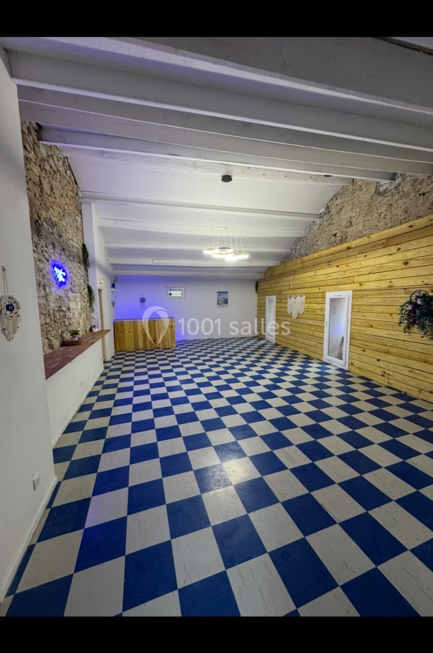 Salle vide avec sol en damier bleu et blanc, murs en pierre et bois, éclairage suspendu et décorations murales.