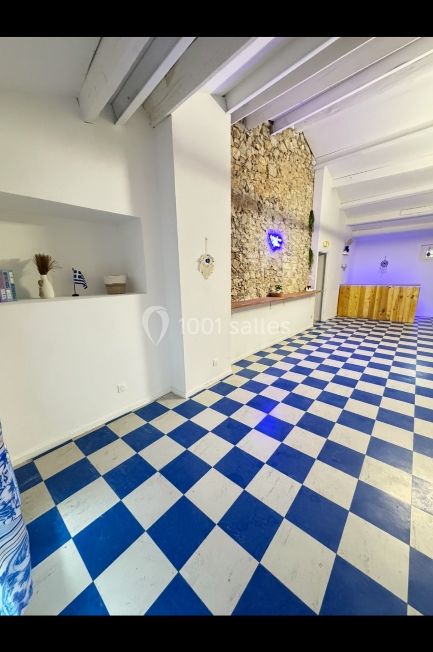 Salle lumineuse avec sol en damier bleu et blanc, mur en pierre, comptoir en bois et décoration minimaliste.