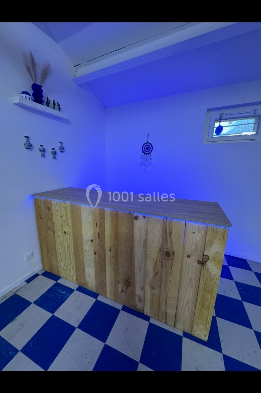 Comptoir en bois clair dans une pièce aux murs blancs, éclairée par une lumière bleue avec un sol à carreaux bleus et blancs.