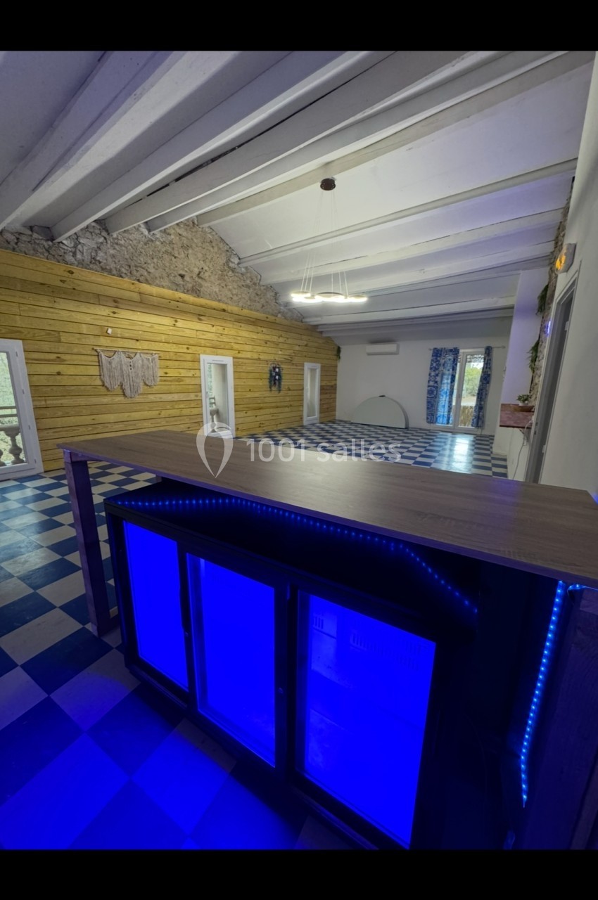 Salle spacieuse avec murs en bois, sol à carreaux bleus et blancs, et un comptoir éclairé par des lumières bleues.