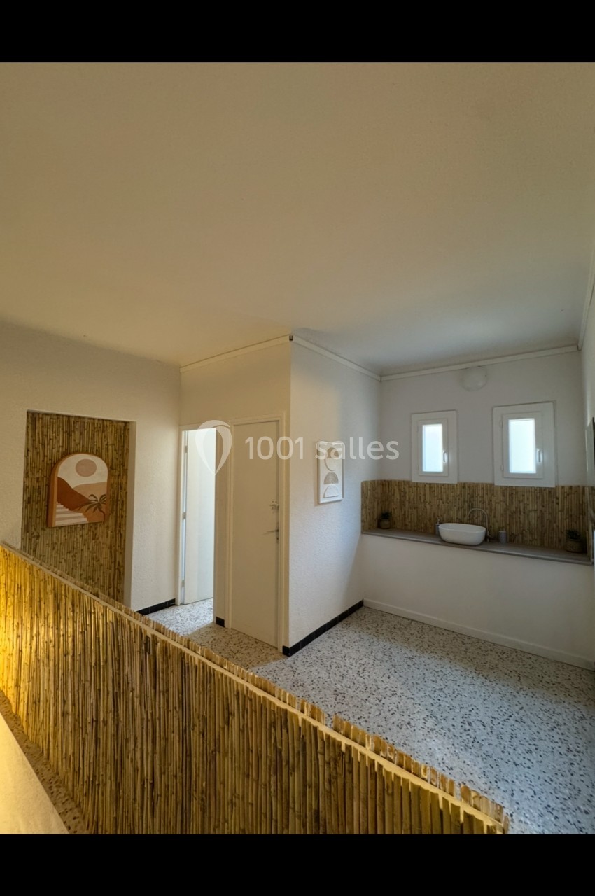 Salle avec cloison en bambou, lavabo moderne, murs blancs, sol en terrazzo et décorations murales minimalistes.