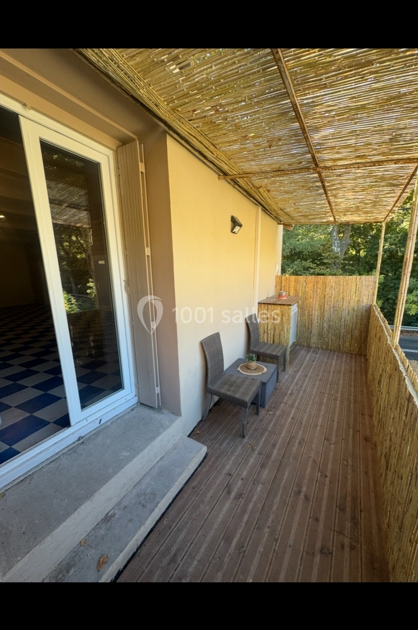 Terrasse en bois avec deux fauteuils, une petite table et un toit en canisse, attenante à une porte-fenêtre.