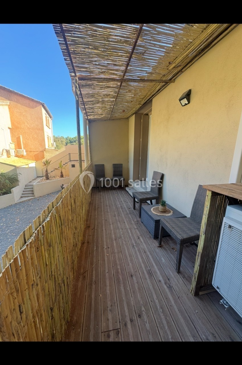Terrasse en bois avec mobilier d'extérieur, pergola en canisse et vue sur des bâtiments voisins sous un ciel dégagé.