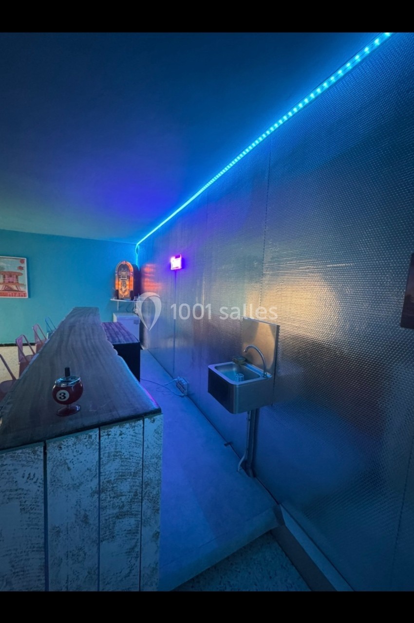 Mur métallique éclairé par des LED bleues, avec un évier et un comptoir en bois dans un espace moderne.
